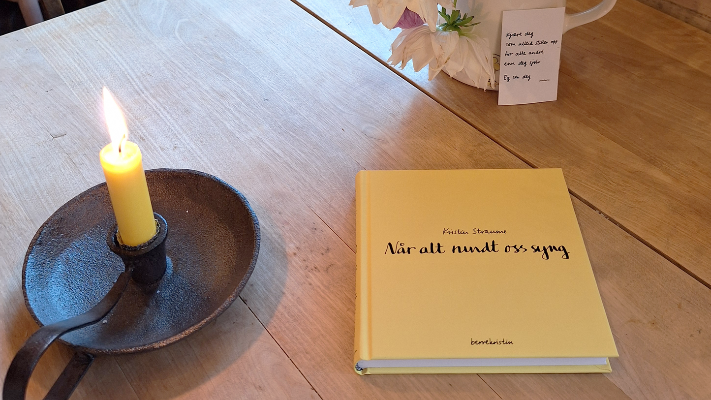 Den gule boka til Kristin Straume, "Når alt rundt oss syng" ligg på eit kafèbord med patina. Ved sida av boka står eit tent lys, sjølvsagt gult det òg. Bakom står ein vakker blomebukett med georginar, i ei gamal mugge.
Lent inntil mugga står eit lite diktkort frå Kristin, med teksten "Kjære deg som alltid stiller opp for alle andre enn deg sjølv. Eg ser deg". Biletet er teke på vakre Aarvik gard i Baldersheim.